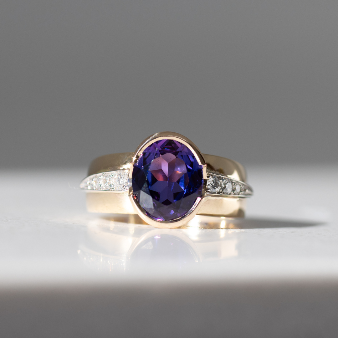 Blue/purple sapphire ring, with a wide tapered band with diamonds set in a white gold shoulder accent